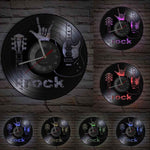 une horloge murale rock en vinyle noir qui montre une guitare, un main avec le signe de la corne et l'heure au centre avec lumièere LED.