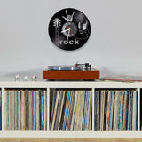 une horloge murale rock en vinyle noir qui montre une guitare, un main avec le signe de la corne et l'heure au centre dans le salon.